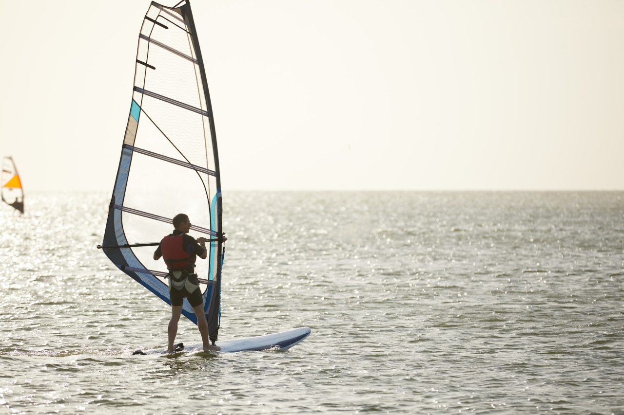 Windsurfer against the backdrop of the setting sun, on calm water, goes calmly along the sea, active